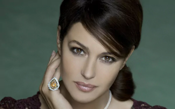 HD wallpaper featuring a brunette Italian actress and model with brown eyes, wearing a ring and gazing confidently. The background is a soft, light green that showcases her elegance.