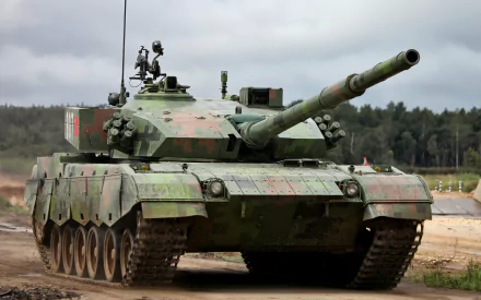 HD PC desktop wallpaper showing a Type 96 military main battle tank in green camouflage, frontal view on a dirt road beneath a cloudy sky.