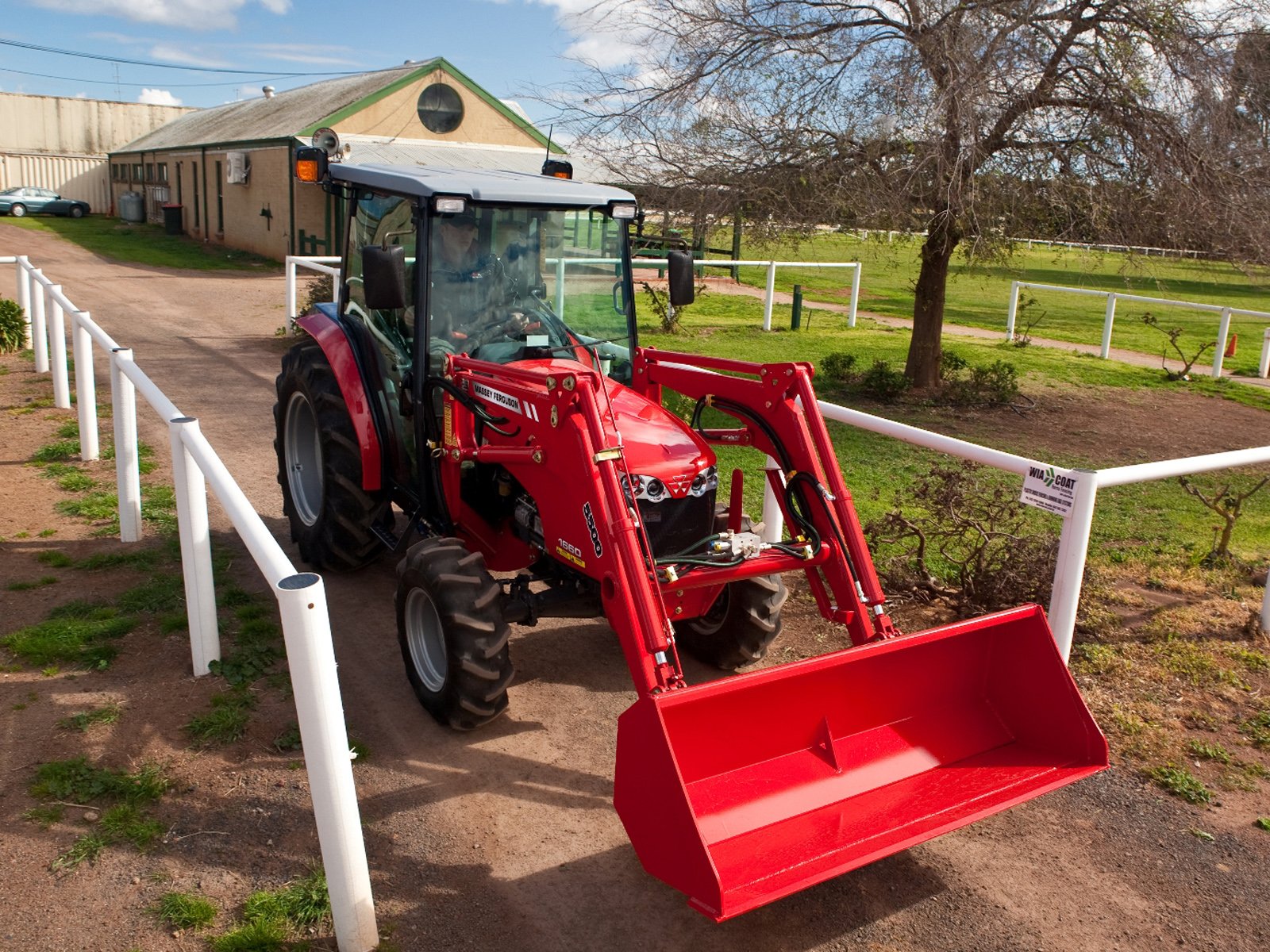 A bright red Massey Ferguson tractor parked on a gravel path, showcasing its powerful front loader against a scenic farm background. An engaging HD desktop wallpaper.