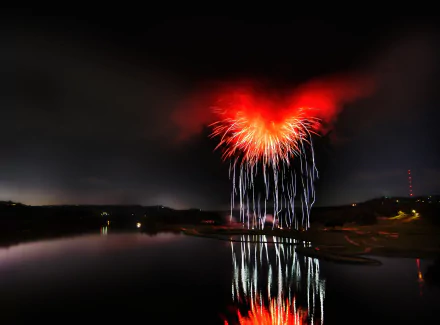 HD photography of vibrant red fireworks illuminating the night sky, reflected on calm water, creating a striking PC desktop wallpaper and background.