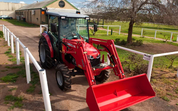 A bright red Massey Ferguson tractor parked on a gravel path, showcasing its powerful front loader against a scenic farm background. An engaging HD desktop wallpaper.