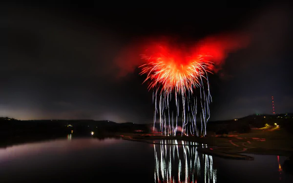 HD photography of vibrant red fireworks illuminating the night sky, reflected on calm water, creating a striking PC desktop wallpaper and background.