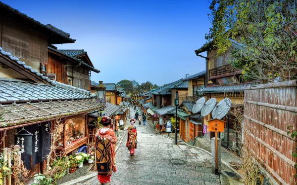 A serene street in Higashiyama, Kyoto, featuring a maiko and a geisha walking past traditional wooden buildings, showcasing the charm of Japan’s cultural heritage.