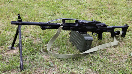 A high-definition wallpaper featuring a machine gun resting on a grassy surface, accompanied by an ammo box, showcasing intricate details of the man-made weaponry.