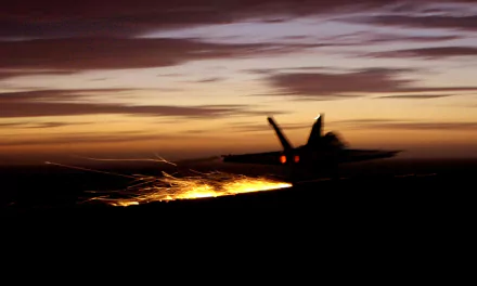HD desktop wallpaper of a McDonnell Douglas F/A-18 Hornet military jet flying with sparks trailing against a dramatic sunset sky.