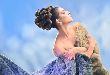 HD desktop wallpaper featuring Indian model Navika Chaudhari with an elaborate hairdo, draped in textured fabrics against a soft blue sky background.