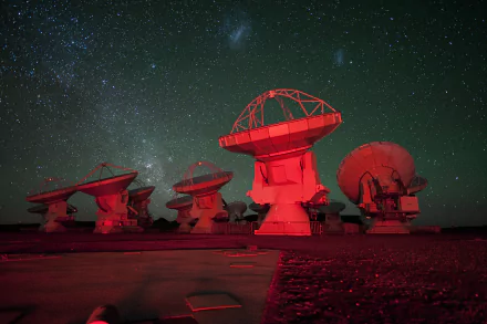 HD desktop wallpaper of ESO’s man-made radio telescope array in Chile’s Atacama Desert: red-lit parabolic dishes under a star-filled sky with the Milky Way.