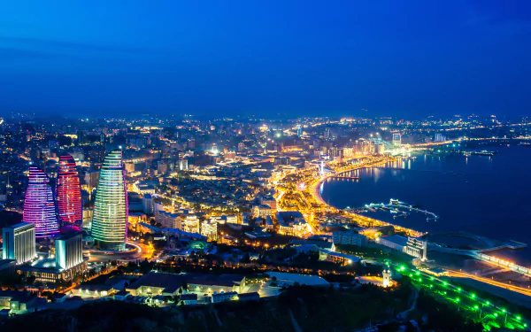 Stunning panoramic view of Baku at night, featuring the iconic Flame Towers illuminated against the city skyline, showcasing Azerbaijan's vibrant urban landscape. Perfect HD desktop wallpaper.