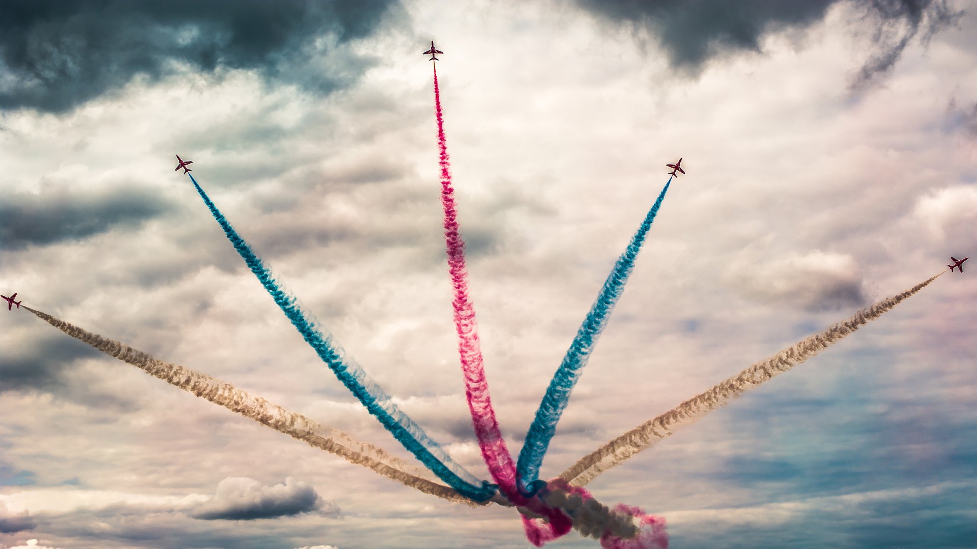 Military aircraft perform an air show in 4K Ultra HD, leaving vibrant blue, red, and white smoke trails against a cloudy sky.