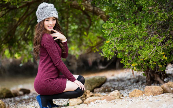 A smiling Asian woman in a cozy outfit poses outdoors near water and greenery, embodying confidence and warmth in this HD wallpaper featuring Jancy Wong.