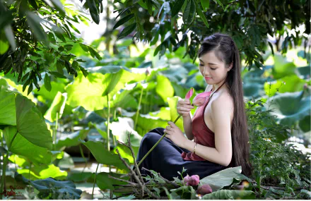 A serene desktop wallpaper featuring a Vietnamese woman in traditional attire, seated by a pond with lotus flowers, surrounded by lush greenery.