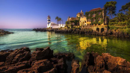 A stunning HD wallpaper depicting a serene sea view with a lighthouse and a villa surrounded by lush greenery and rocky shores, capturing the tranquil beauty of coastal life.