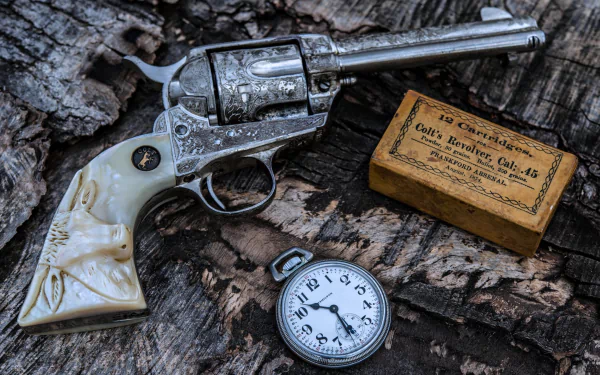 A detailed Colt revolver rests on a wooden surface alongside a vintage watch and a wooden box labeled for Colt Revolver .45 cartridges.