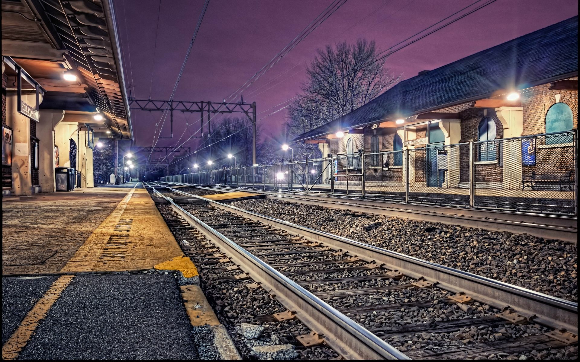 HD PC desktop wallpaper and background showing a man-made railroad station at night: empty platforms, converging tracks and glowing station lights beneath a purple sky.