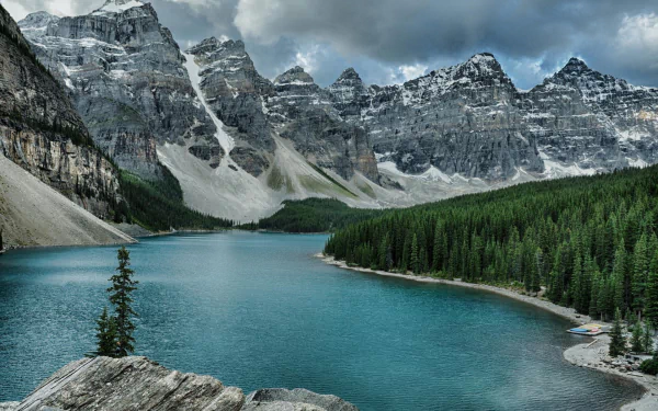 Stunning view of Moraine Lake surrounded by majestic peaks in Banff National Park, Alberta. The vibrant blue water contrasts beautifully with the lush green forests and rocky mountains.