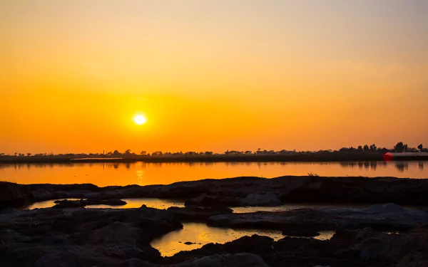 Sunset over a serene lake in Pakistan, showcasing a vibrant orange sky reflecting on calm waters in this 4K Ultra HD nature landscape wallpaper.