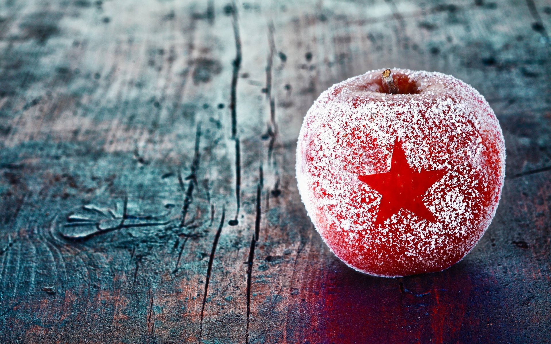 HD desktop wallpaper featuring a frozen apple dusted with frost, sitting on a textured wooden surface with a red star design on the fruit.