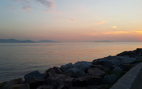 5K Ultra HD photography sunset: calm coastal seascape with pastel sky, distant mountains and rocky shoreline, PC desktop wallpaper and background.