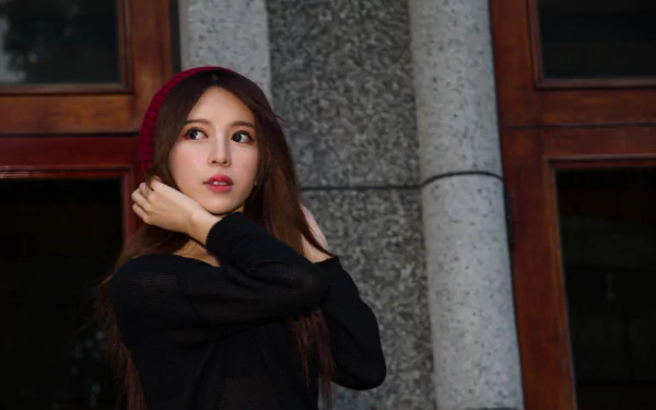 Female model posing by a stone column and wooden window, wearing a red knit hat and black top — 4K Ultra HD PC desktop wallpaper.