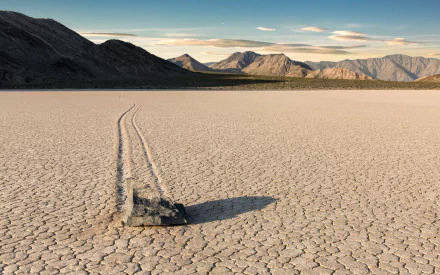Death Valley nature HD PC desktop wallpaper and background: a lone sliding rock leaves a long trail across a cracked dry playa toward distant mountains under a wide clear sky.