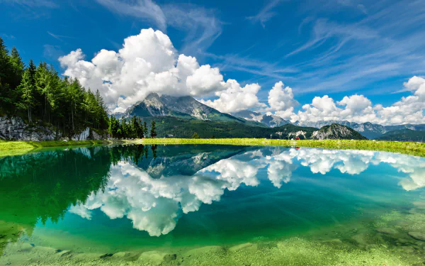 HD desktop wallpaper featuring a breathtaking nature scene with a clear mountain lake reflecting fluffy white clouds and a vivid blue sky.