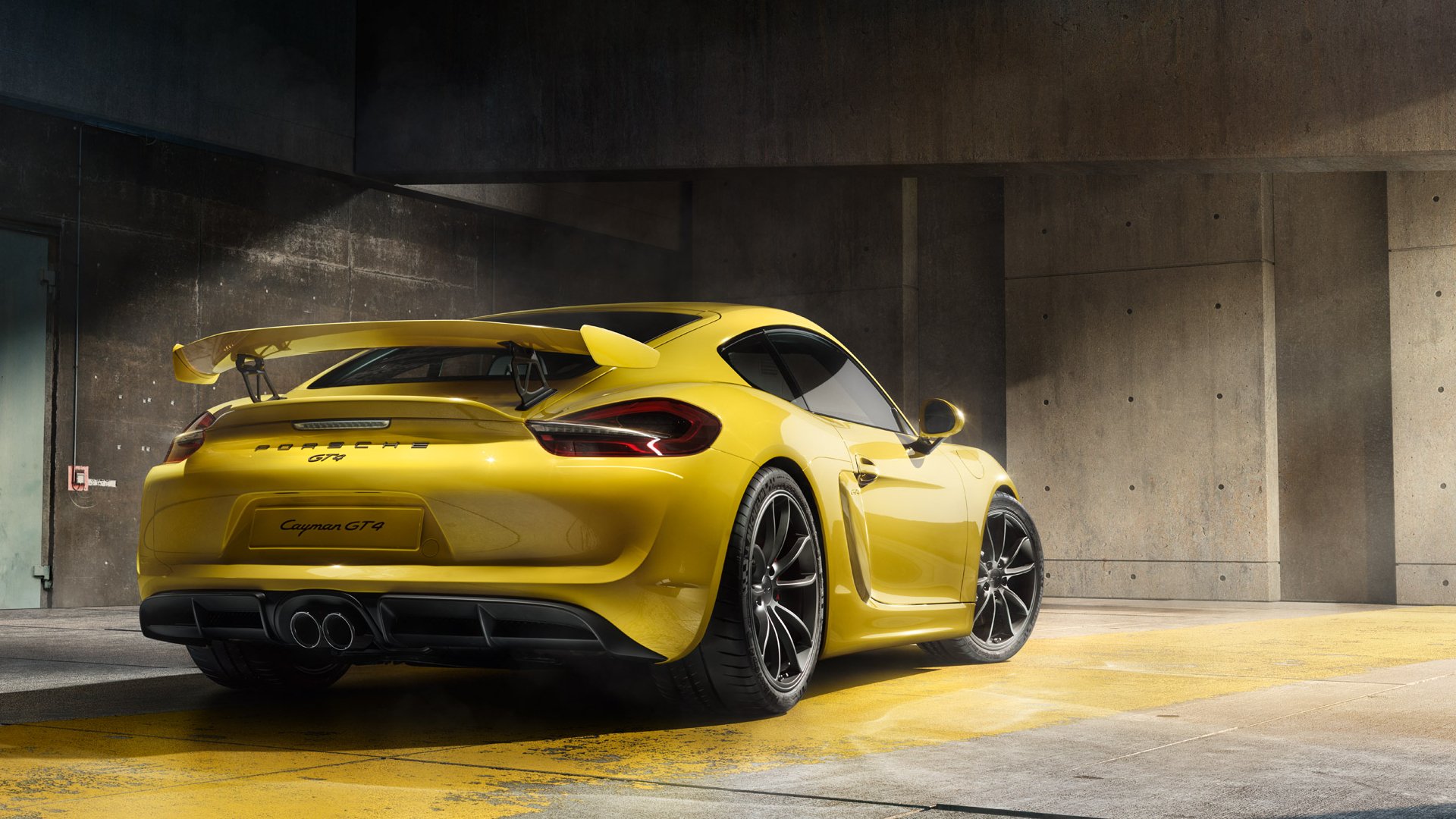Yellow Porsche Cayman GT4 sports car parked in a modern concrete garage, showcased as an HD PC desktop wallpaper and background.
