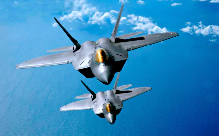 Two Lockheed Martin F-22 Raptors soar through a clear blue sky, showcasing their sleek design and military prowess, creating a striking HD desktop wallpaper.
