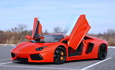 An eye-catching orange Lamborghini Aventador LP700-4 features striking scissor doors, showcasing its sleek design and powerful stance in a vibrant outdoor setting.