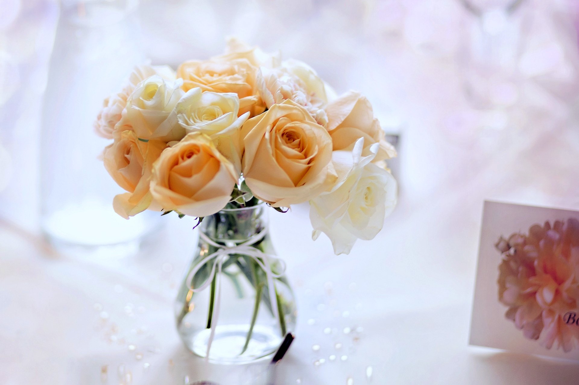 4K Ultra HD still-life photo of pale peach and cream roses in a clear glass vase on a softly lit table with dreamy bokeh — PC desktop wallpaper background.