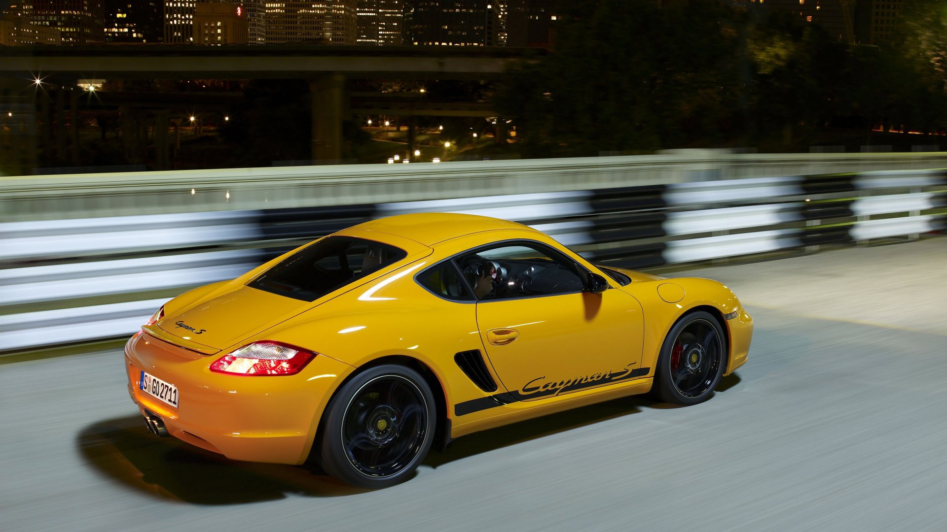 Yellow Porsche Cayman S sports car speeding on a city road at night, side view; 2K Quad HD PC desktop wallpaper and background.