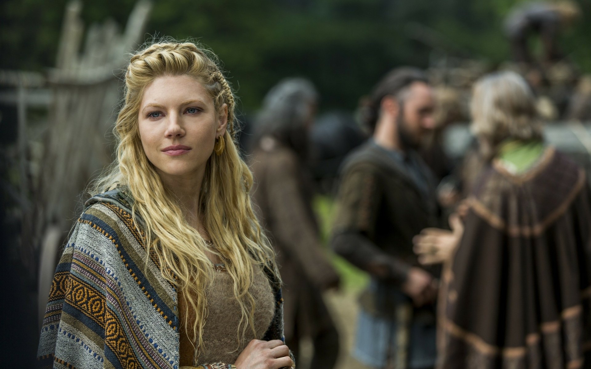 Lagertha, portrayed by Canadian actress Katheryn Winnick in the TV show Vikings (2013), stands confidently with her striking blue eyes and blonde hair, surrounded by fellow characters.