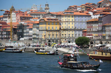 Colorful houses line the quay along the river in Porto, Portugal, with boats on the water and a crane visible in the vibrant 4K Ultra HD cityscape background.
