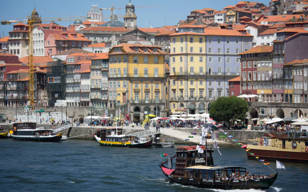 Colorful houses line the quay along the river in Porto, Portugal, with boats on the water and a crane visible in the vibrant 4K Ultra HD cityscape background.