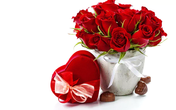 A vibrant arrangement of red roses in a vase beside a heart-shaped box of chocolates, symbolizing love and romance. This HD image serves as an elegant desktop wallpaper.