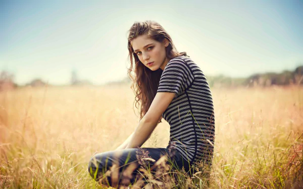 A serene outdoor portrait of Birdy, the English singer, sitting in a golden field. The soft lighting highlights her contemplative expression, creating a captivating music-inspired atmosphere.