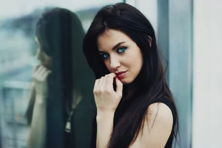 HD desktop wallpaper of a brunette woman with blue eyes, posing near a reflective surface. The image captures her intense gaze and reflective counterpart.