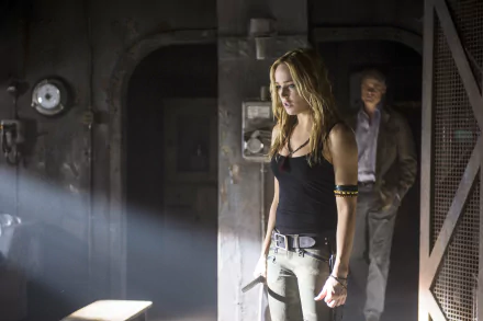 HD PC desktop wallpaper featuring Caity Lotz from the TV show Arrow, standing in a dimly lit industrial setting with beams of light highlighting her figure.