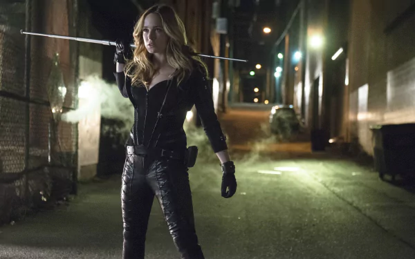 Caity Lotz as Black Canary poses confidently in a dimly lit alley, wielding a weapon, showcasing her fierce character from the TV show Arrow. HD wallpaper background.