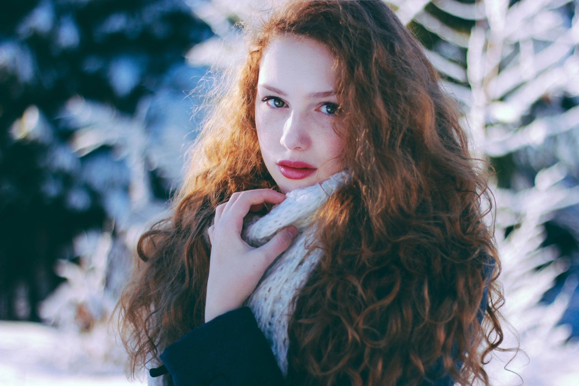 HD desktop wallpaper of a redhead woman with green eyes and freckles, wearing a cozy scarf, set against a blurred snowy background.