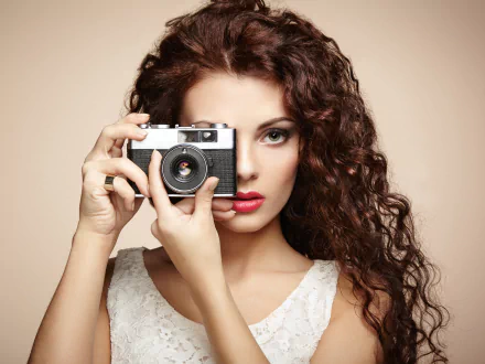 HD desktop wallpaper of a woman with curly hair holding a vintage camera up to her eye, striking a pose.