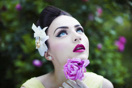 A brunette woman with blue eyes and bold lipstick gazes upwards while holding a pink flower, set against a vibrant green background, creating a striking HD desktop wallpaper.