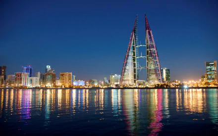 Manama night skyline with the twin Bahrain World Trade Center skyscrapers lit and reflected on calm water, colorful city lights along the man-made waterfront — HD PC desktop wallpaper