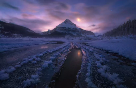 A serene night landscape of the Canadian Rockies in Alberta, featuring a moonlit scene with snow, ice, and a winding waterway, capturing the beauty of winter nature.