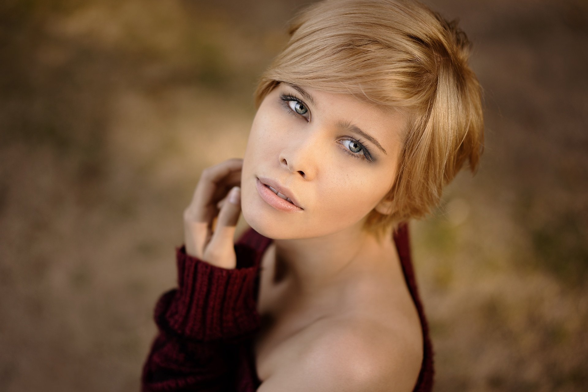 HD desktop wallpaper featuring a blonde woman with striking blue eyes and short hair, set against a softly blurred bokeh background.