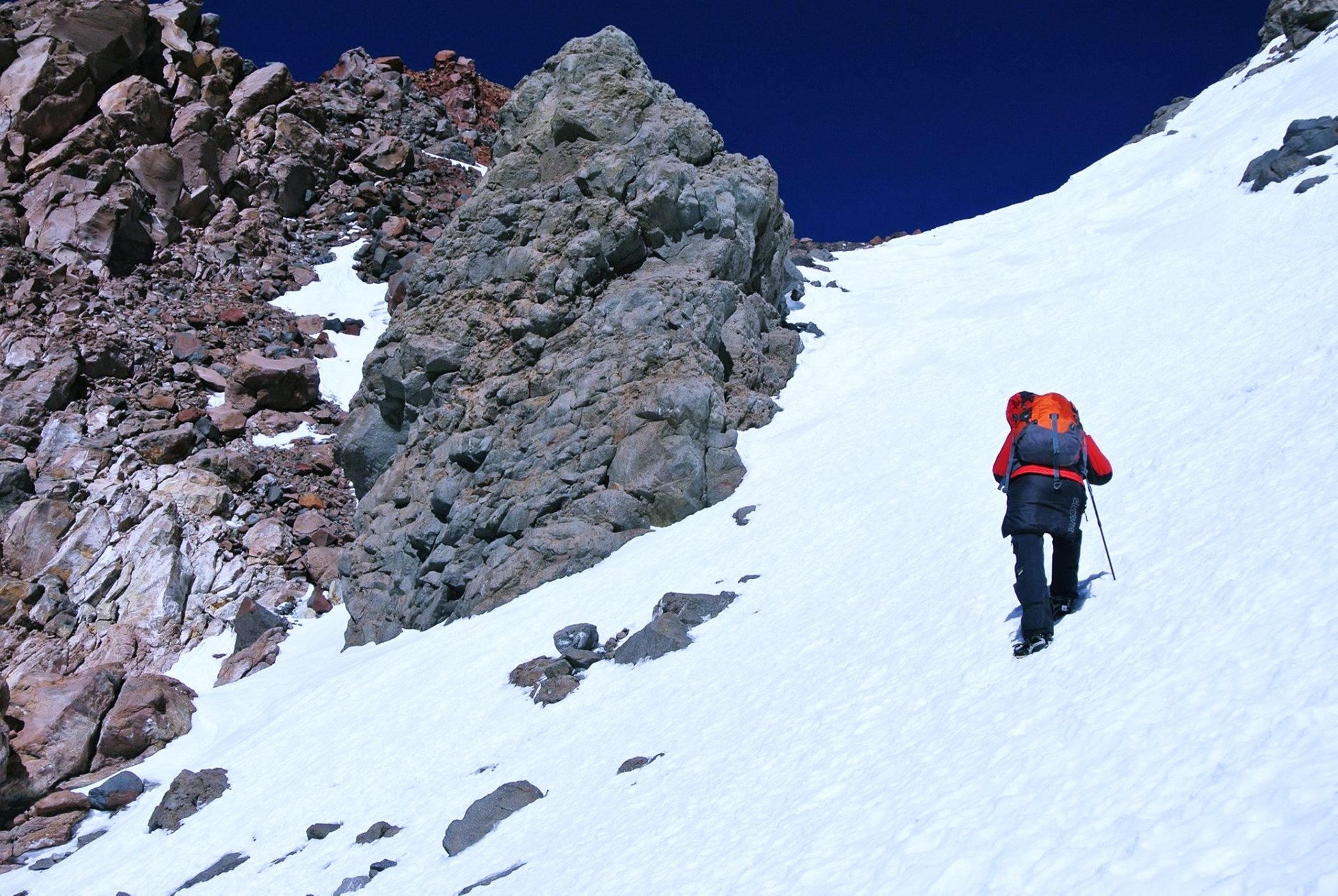 4K Ultra HD PC wallpaper: mountaineer in red jacket climbs a stone-strewn snowy mountain slope under a deep blue sky — winter nature, snow sports scene.