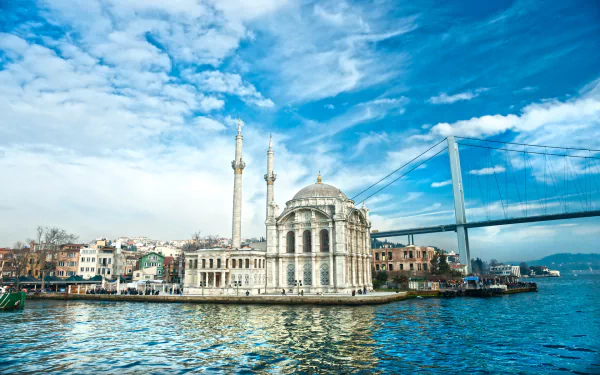 A stunning HD image of Istanbul featuring the ornate Ortaköy Mosque beside a glistening waterfront and the Bosphorus Bridge under a bright, blue sky. A captivating man-made landscape.