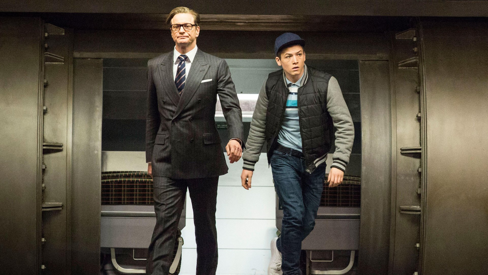 Taron Egerton and Colin Firth walk confidently through a sleek, modern setting in a scene from Kingsman: The Secret Service, captured in stunning 4K Ultra HD.