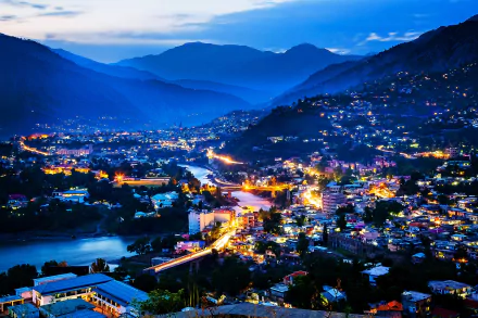Nighttime cityscape of a vibrant man-made settlement in Kashmir, Pakistan, nestled between mountains and a river, captured in stunning 4K Ultra HD detail.