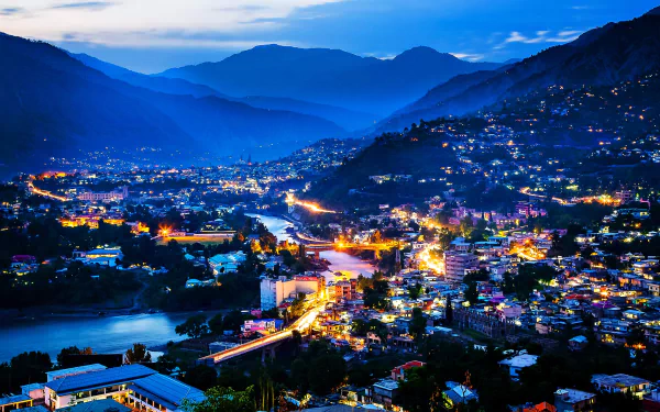 Nighttime cityscape of a vibrant man-made settlement in Kashmir, Pakistan, nestled between mountains and a river, captured in stunning 4K Ultra HD detail.