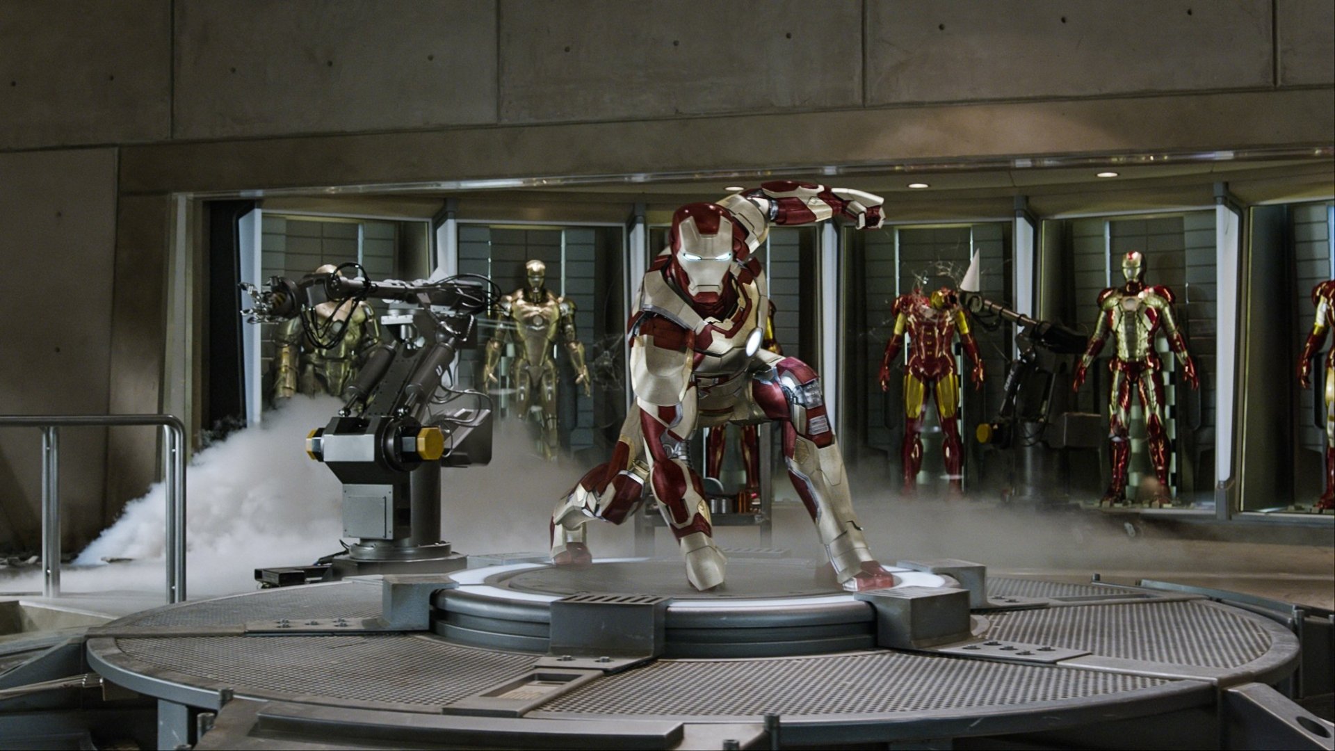 HD PC desktop wallpaper from the Iron Man 3 movie: Iron Man in red-and-gold armor kneels on a lit platform in his workshop, with multiple suits displayed behind.